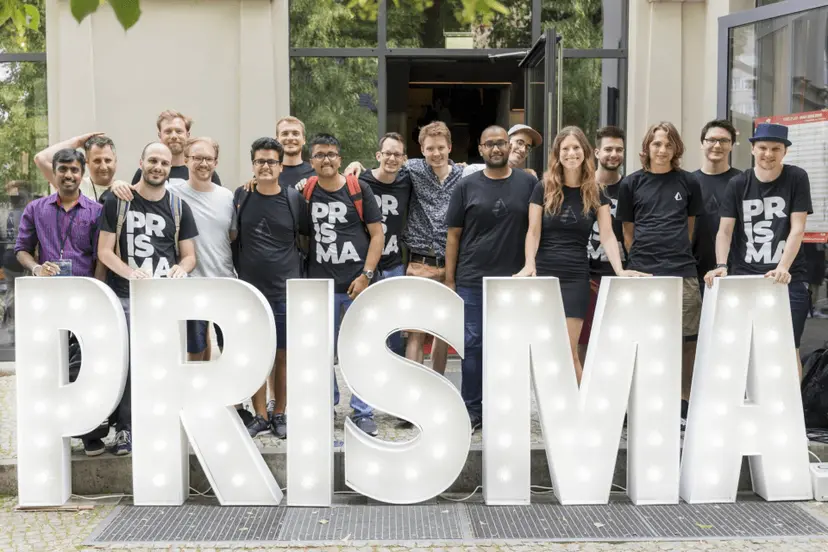 Prisma team members posing in front of illuminated PRISMA lettering